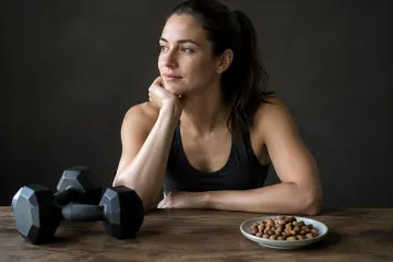 Femme sportive pensive, haltères devant elle et petite assiette de noix sur table